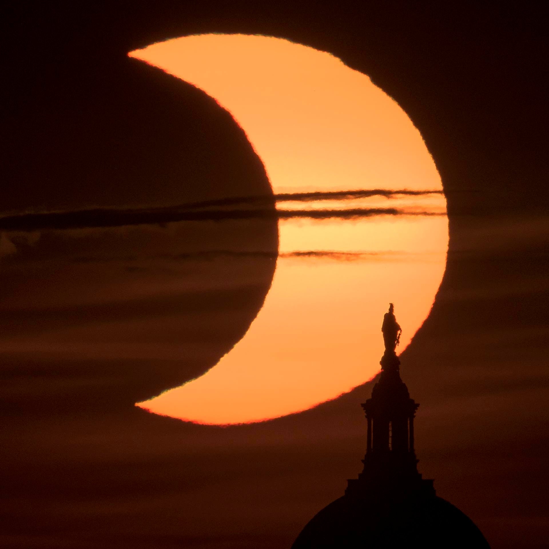 A partial solar eclipse is seen as the sun rises behind the Statue of Freedom atop the United States Capitol Building, Thursday, June 10, 2021, as seen from Arlington, Virginia. Credit: NASA/Bill Ingalls